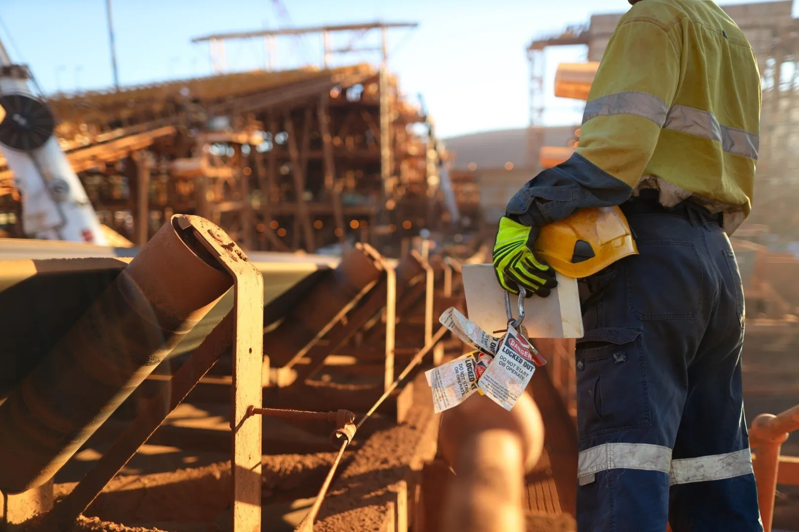 Construction worker holding a hard hat and lockout tags on an industrial site
